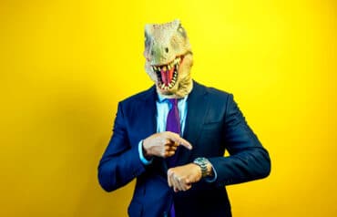 dinosaur head on businessman pointing at his watch