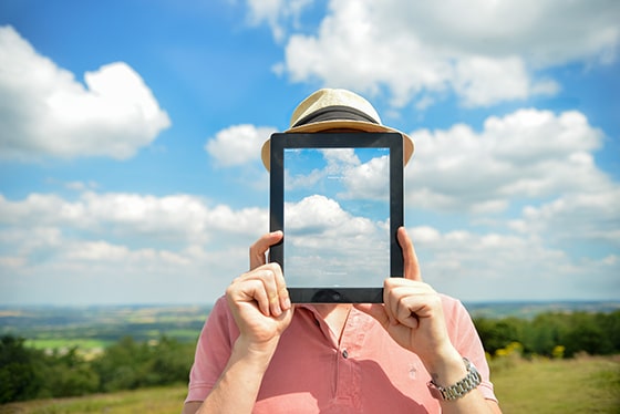 Concept Of Man Holding iPad In Front Of Face With Clouds And Countryside