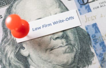 Close-up of a $100 bill with a red pin holding a note that reads Law Firm Write-Offs.