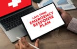 A person holding a tablet displaying a law firm emergency plan next to a laptop and charts.
