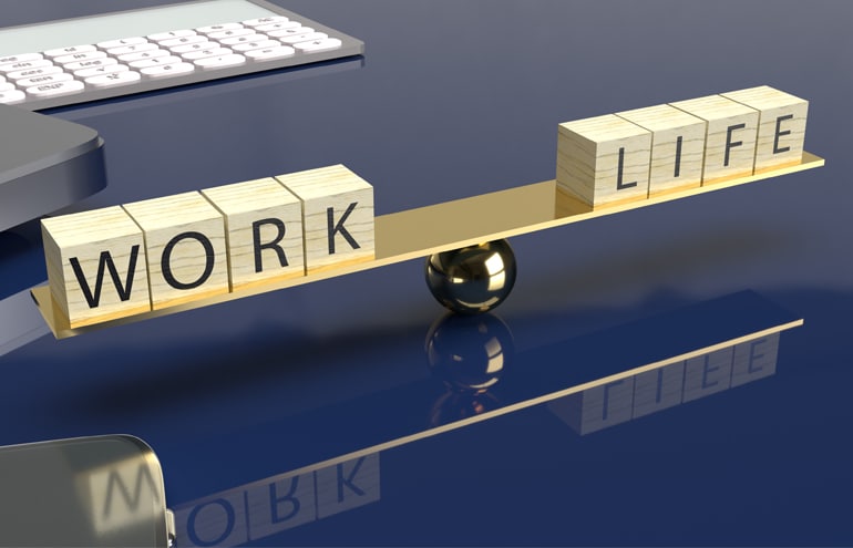 Wooden blocks spelling work and life balanced on a seesaw scale for law practice well-being strategy.