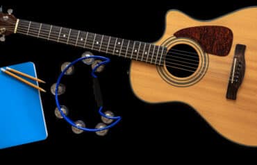 Acoustic guitar, tambourine, and notebook on a black background, illustrating creative hobbies for lawyers to reduce stress.