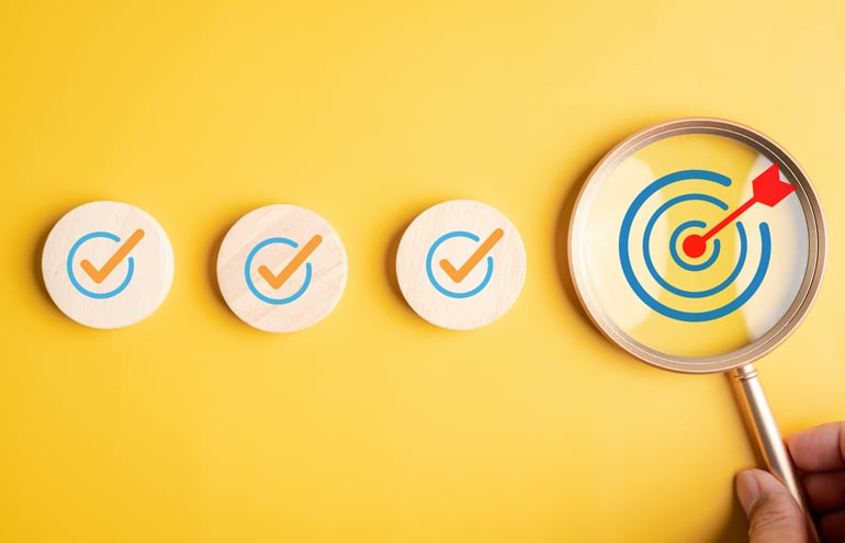 Magnifying glass focusing on a bullseye target next to checked wooden blocks, representing a comprehensive law firm startup checklist.
