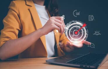 A lawyer in a mustard jacket pointing to a glowing target icon on a laptop screen, representing law firm sales professionals setting business development goals.